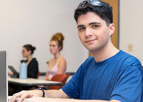  'Male' student with blue shirt typing on a laptop